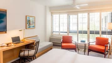 A hotel room with a bed, desk, laptop, chair, and two armchairs.