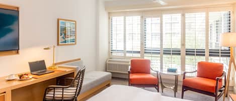 A hotel room with a bed, desk, laptop, chair, and two armchairs.