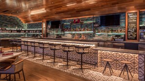 Zona de bar con una barra larga, varios taburetes y una variedad de botellas y vasos en estanterías.