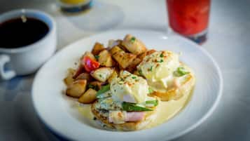 A plate of food with poached eggs, greens, and potatoes, accompanied by a cup of coffee and a glass of red drink.