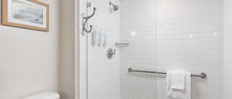 Un baño moderno con azulejos blancos tipo metro, cabina de ducha de vidrio, inodoro, toallero y un cuadro en la pared.