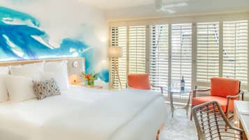 Habitación de hotel con una cama grande, un escritorio con dos sillas, una ventana con persianas y un ventilador de techo.