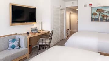 A hotel room with a bed, a desk with a laptop, a chair, a TV, and a painting on the wall.
