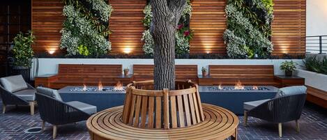Een buitenzitplaats met een houten bank, stoelen en een centraal vuurkorf.