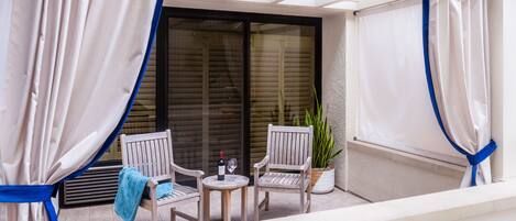 A balcony with two wooden chairs, a small table, a bottle of wine, and a glass.