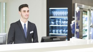 A hotel reception area with a modern design, a reception desk, and a display of various items in the background. - NH Brussels Grand Place Arenberg (Brussels)