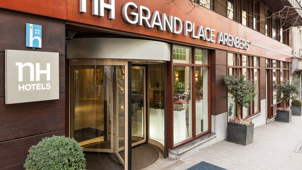 The exterior of NH Grand Place Arenberg hotel with a revolving door entrance, large windows, and potted plants. - NH Brussels Grand Place Arenberg (Brussels)
