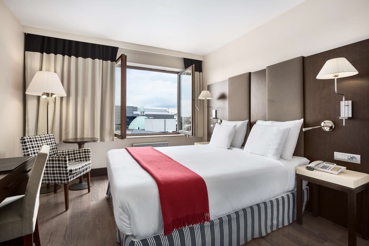 Habitación de hotel con una cama grande, un escritorio, una silla y una ventana con cortinas.
