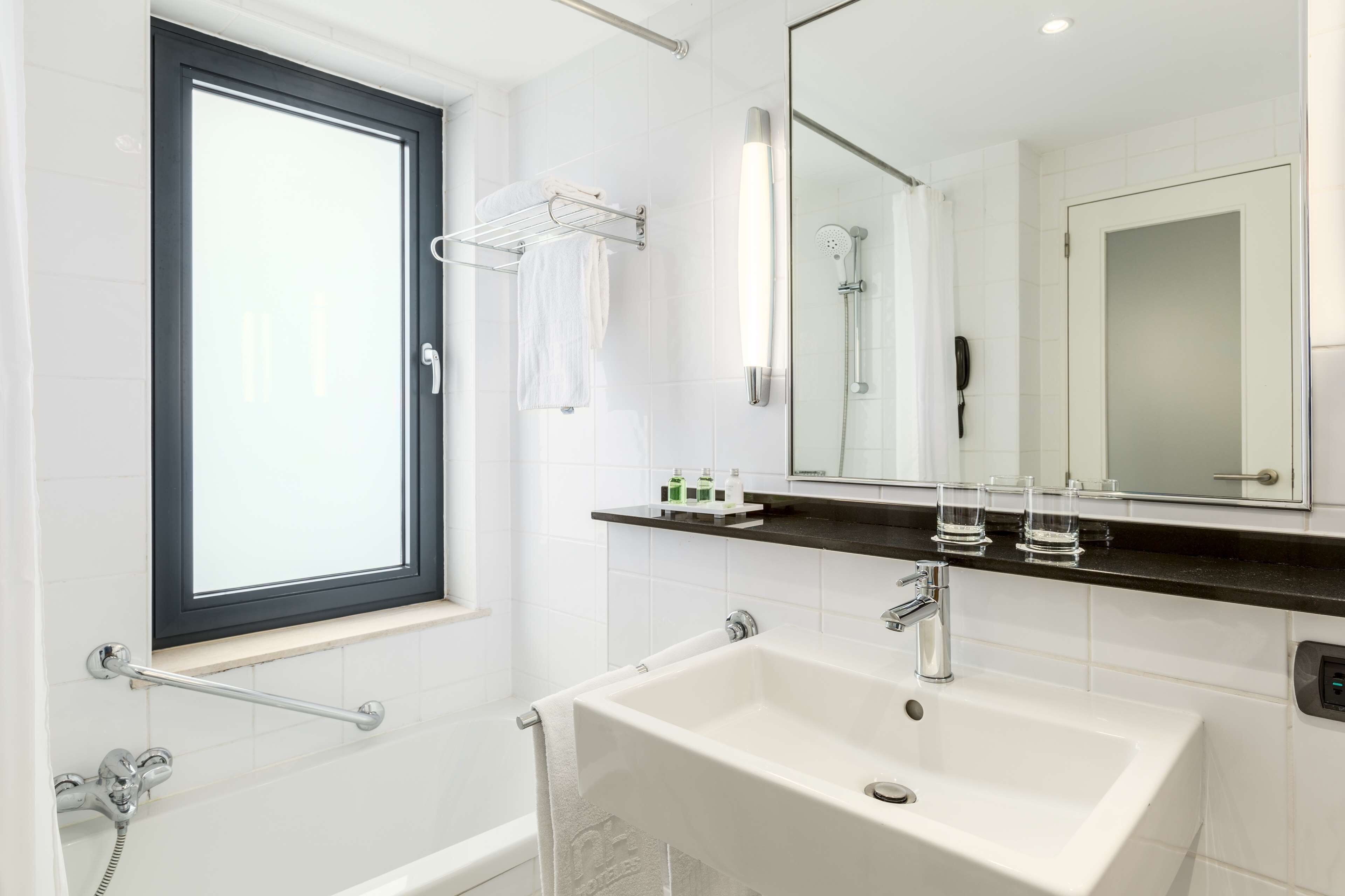 Une salle de bain moderne dotée d’une grande fenêtre, d’une baignoire, d’un lavabo et d’un miroir.