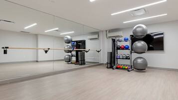 Un gimnasio con espejo, pelotas de ejercicio y un estante con mancuernas de colores.