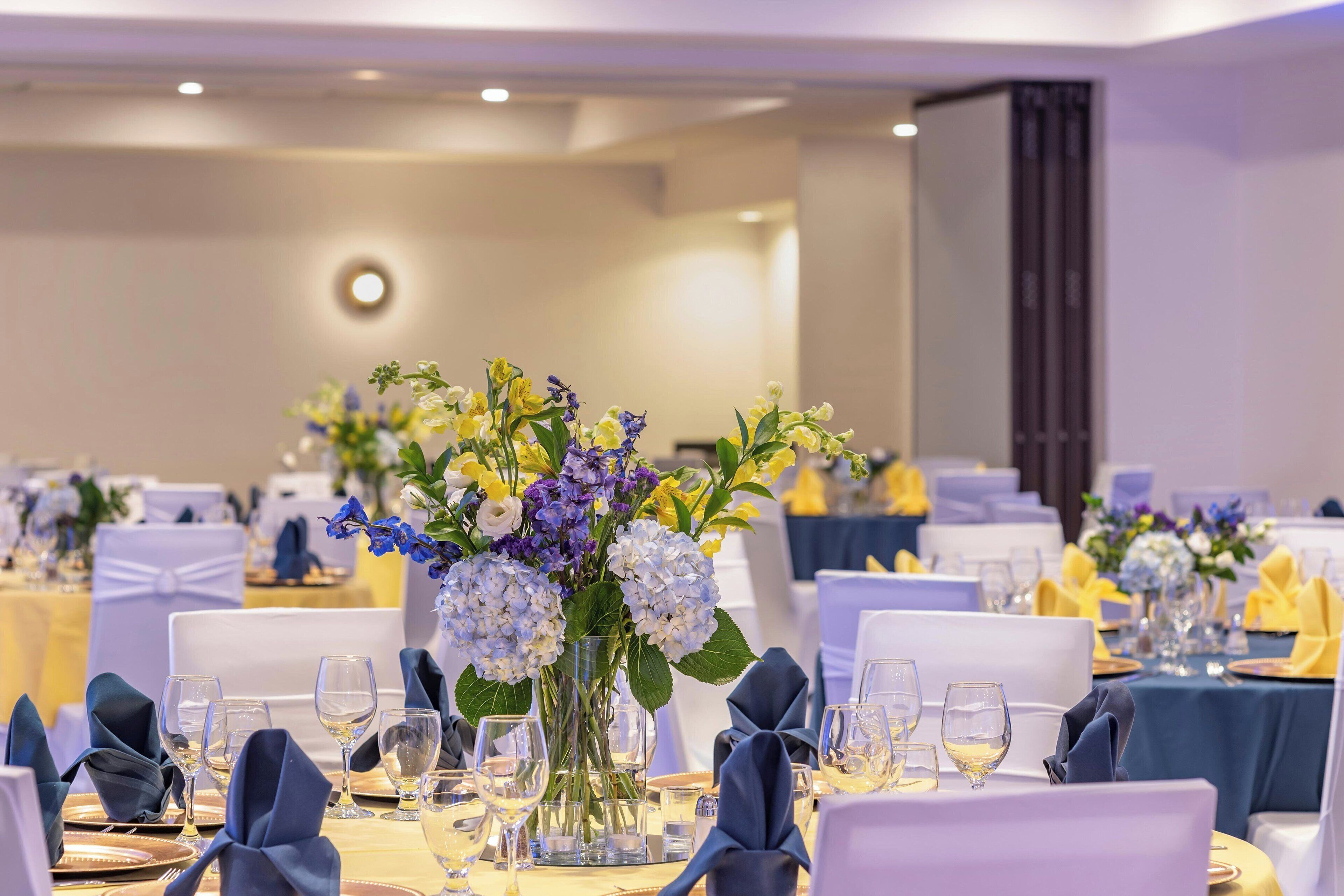 Une salle de banquet avec des tables rondes dressées pour le repas, agrémentées de compositions florales et d’une décoration de table soignée.