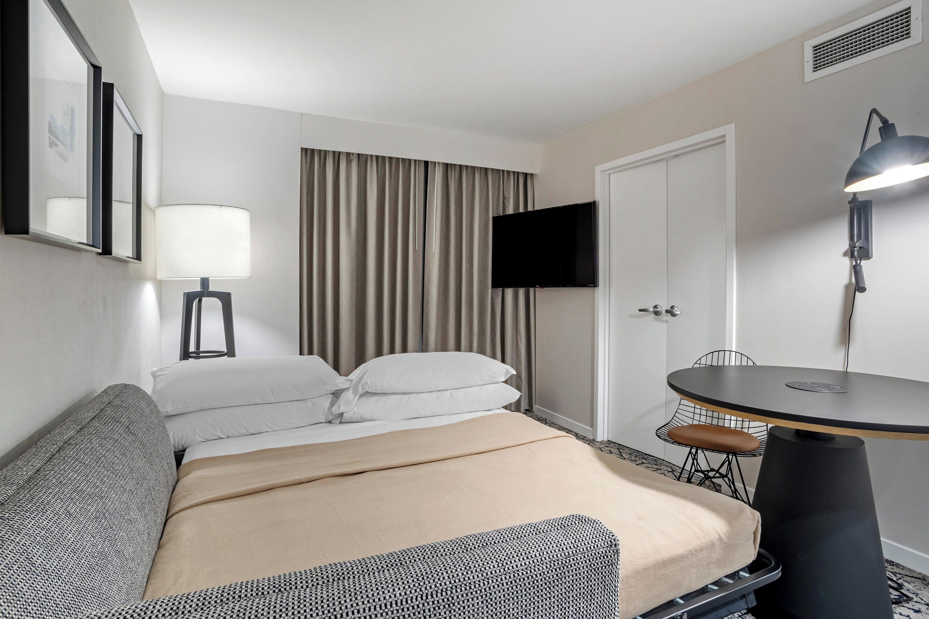 Una habitación de hotel con cama, escritorio, silla, televisor y lámpara.