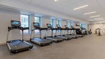 Un gimnasio con varias caminadoras alineadas, ventanas amplias y un diseño moderno y limpio.