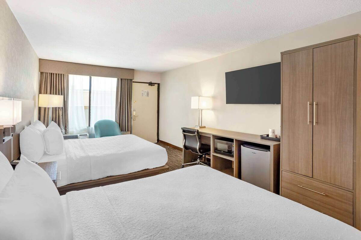 Een hotelkamer met twee bedden, een bureau, een stoel, een televisie en een kledingkast.