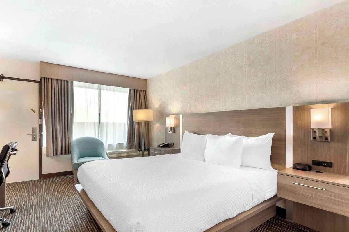 Een hotelkamer met een groot bed, een bureau met lamp, een stoel en een raam met gordijnen.