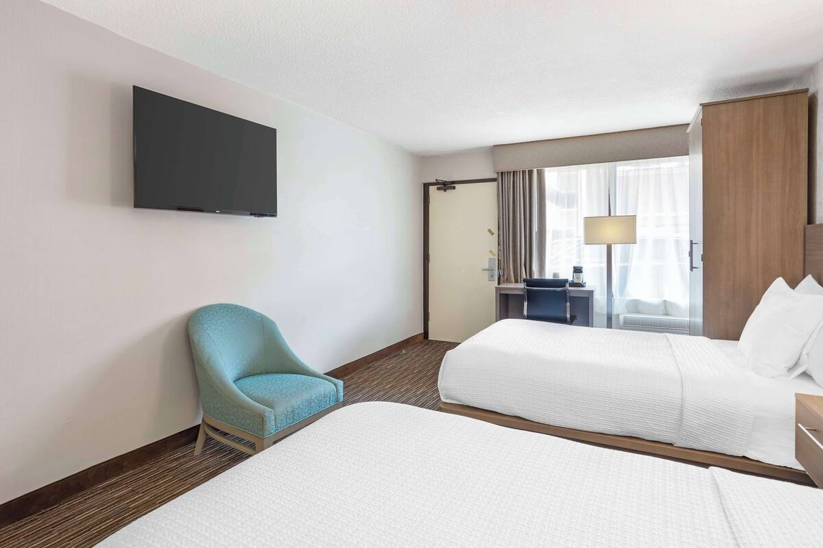 Een hotelkamer met twee bedden, een aan de muur bevestigde televisie, een bureau met een lamp en een stoel.
