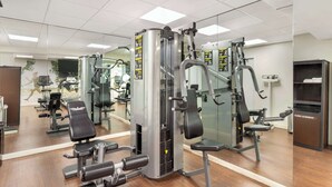 Un gimnasio con diversas máquinas de ejercicio, un muro de espejos y una pantalla de televisión.