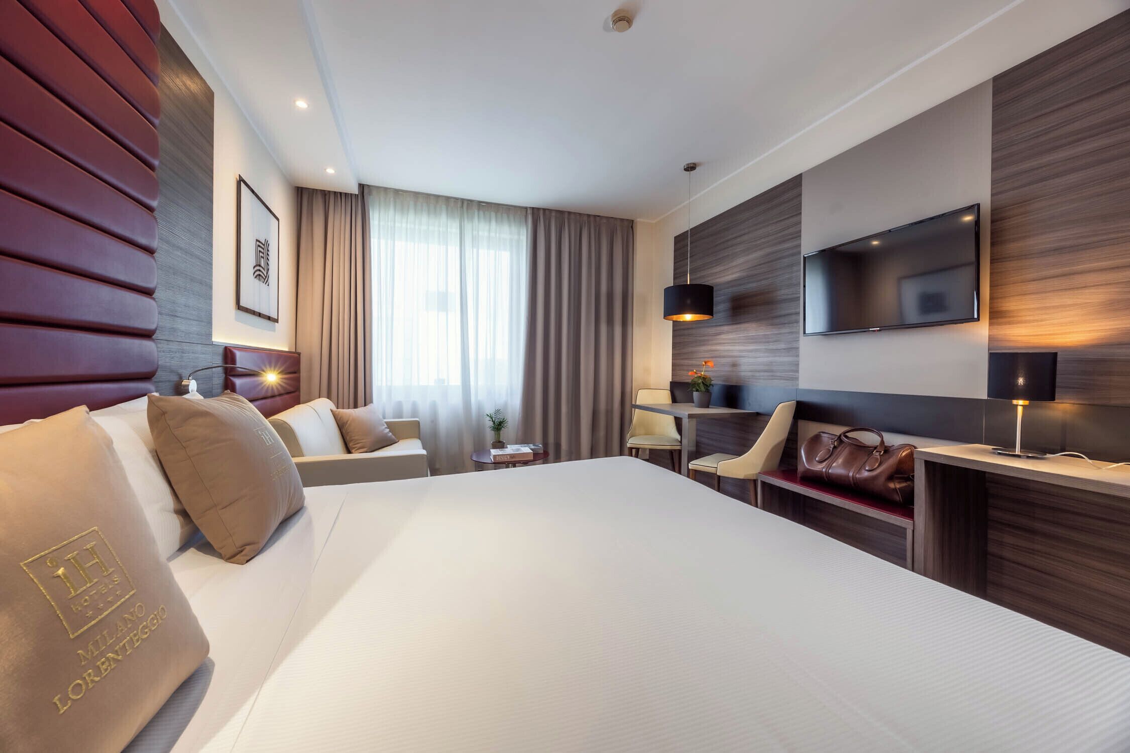A hotel room with a large bed, a desk, a TV, and a seating area with a chair and a table.