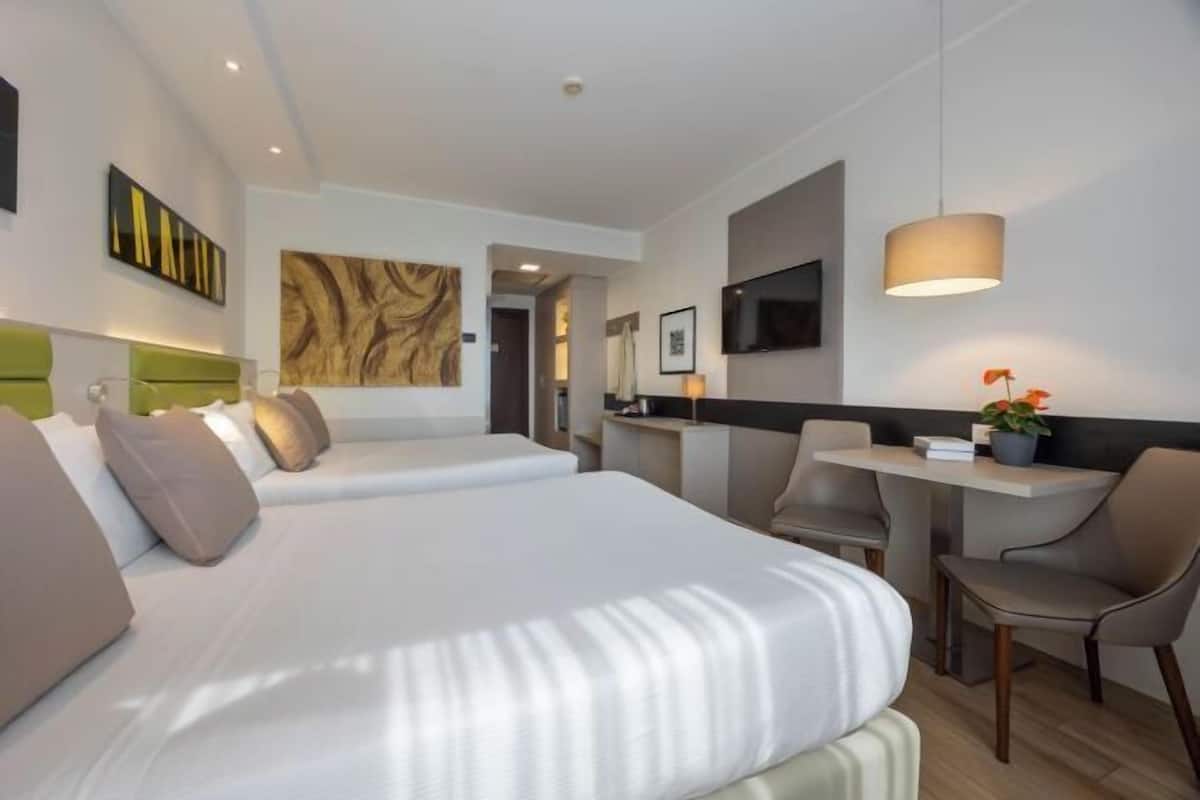 A modern hotel room with a large bed, a desk, a chair, and a TV.