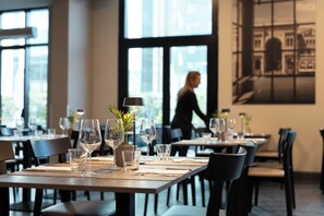 A restaurant interior with tables set for dining, large windows, and a cityscape view. - iH Hotels Milano Lorenteggio (Milan)