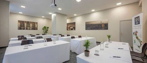 A conference room with multiple tables, ceiling-mounted projectors, and framed artwork on the walls.