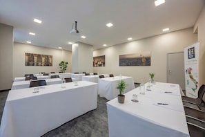 Un salón de conferencias con varias mesas, proyectores instalados en el techo y obras de arte enmarcadas en las paredes.