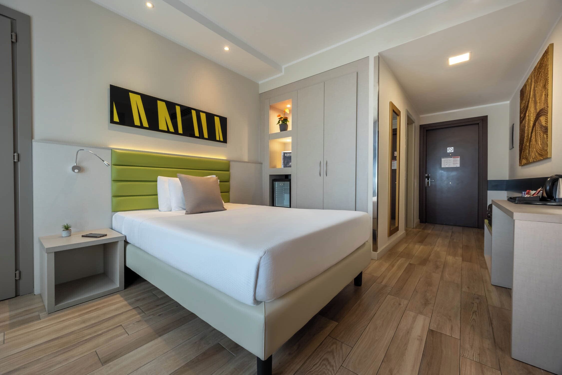 Una habitación de hotel moderna con cama, mesita de noche, armario y un pequeño escritorio.