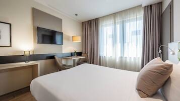 Een hotelkamer met een bed, een bureau, een stoel, een televisie en een raam met gordijnen.