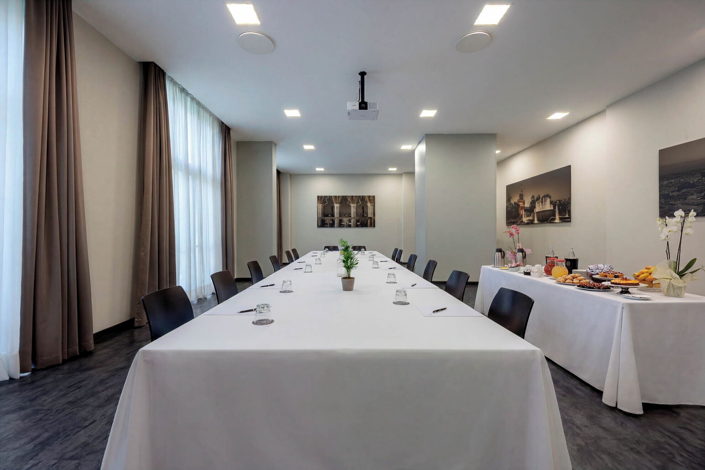 A conference room with a long table, chairs, a projector, and a buffet table with food and flowers.