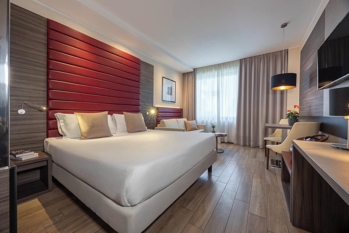 A modern hotel room with a large bed, a desk, a chair, and a TV.