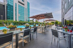 An outdoor dining area with tables and chairs, a pool, and modern buildings in the background. - iH Hotels Milano Lorenteggio (Milan)