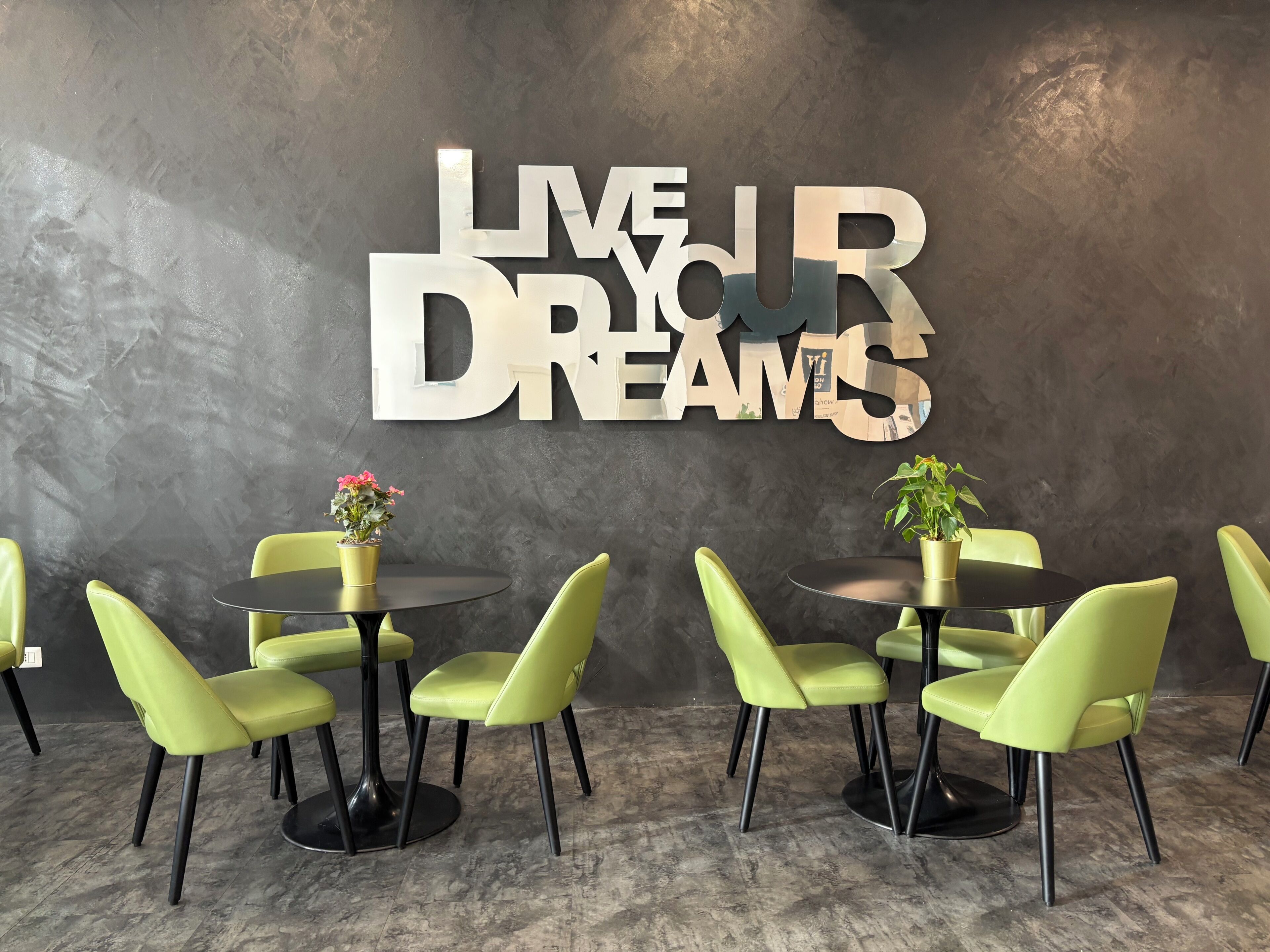 A modern interior with a motivational wall sign, green chairs, and round tables.