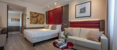 Una habitación de hotel moderna con una cama, un sofá, una mesita y una obra de arte colgada en la pared.