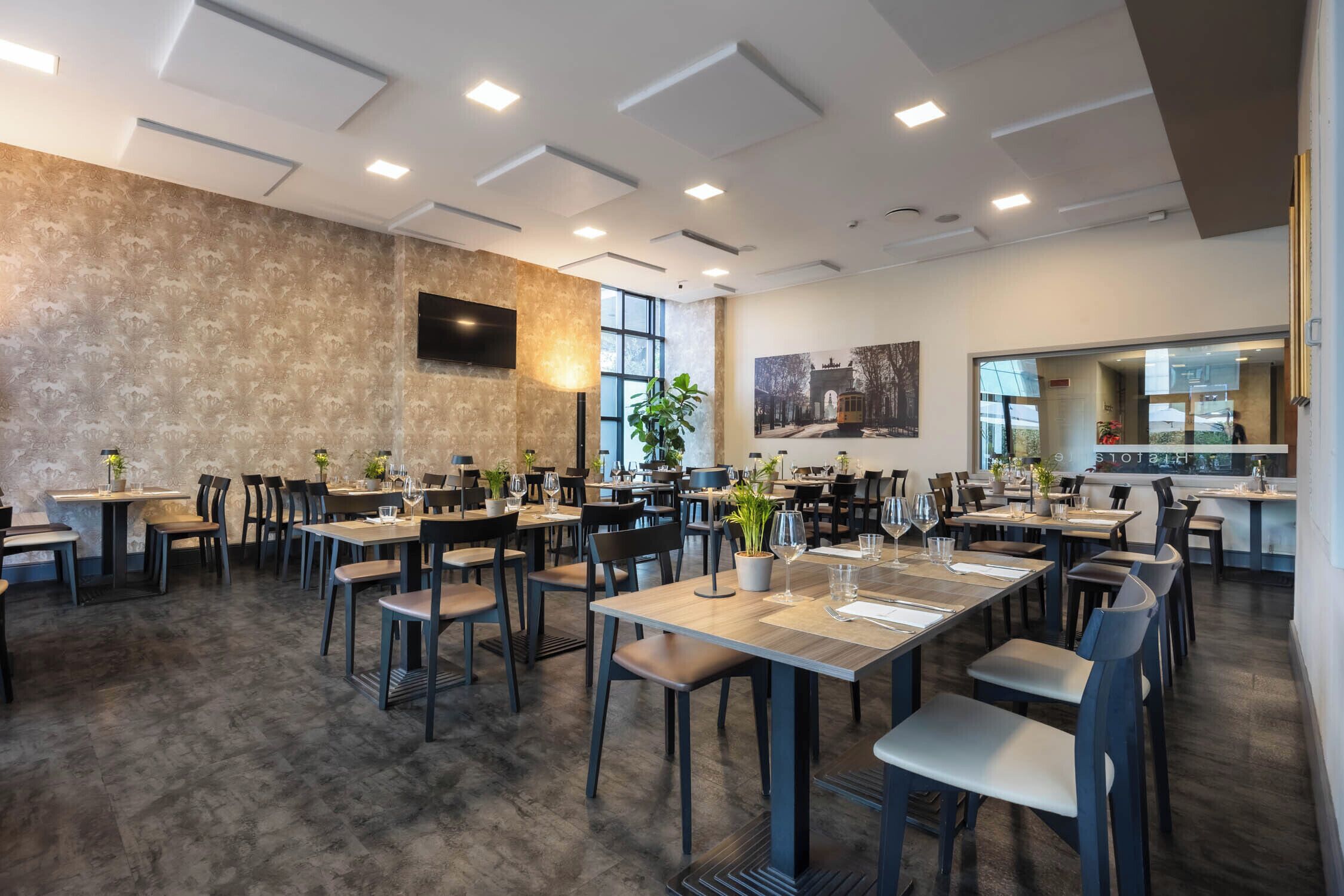 A spacious dining area with multiple tables and chairs, a large window, and a mounted television on the wall.