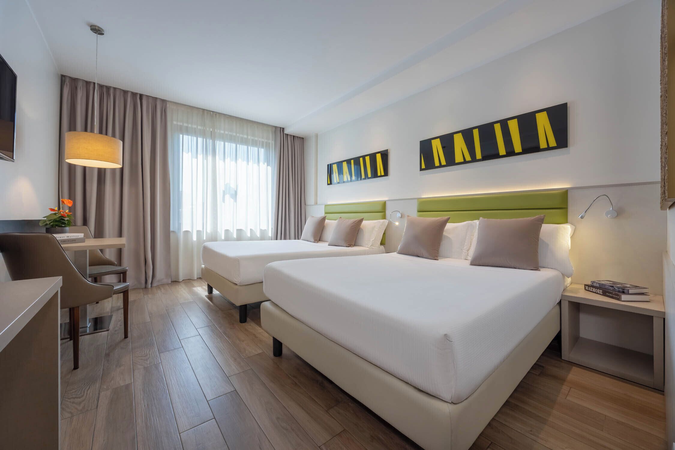 A hotel room with two beds, a desk, a chair, and a lamp.
