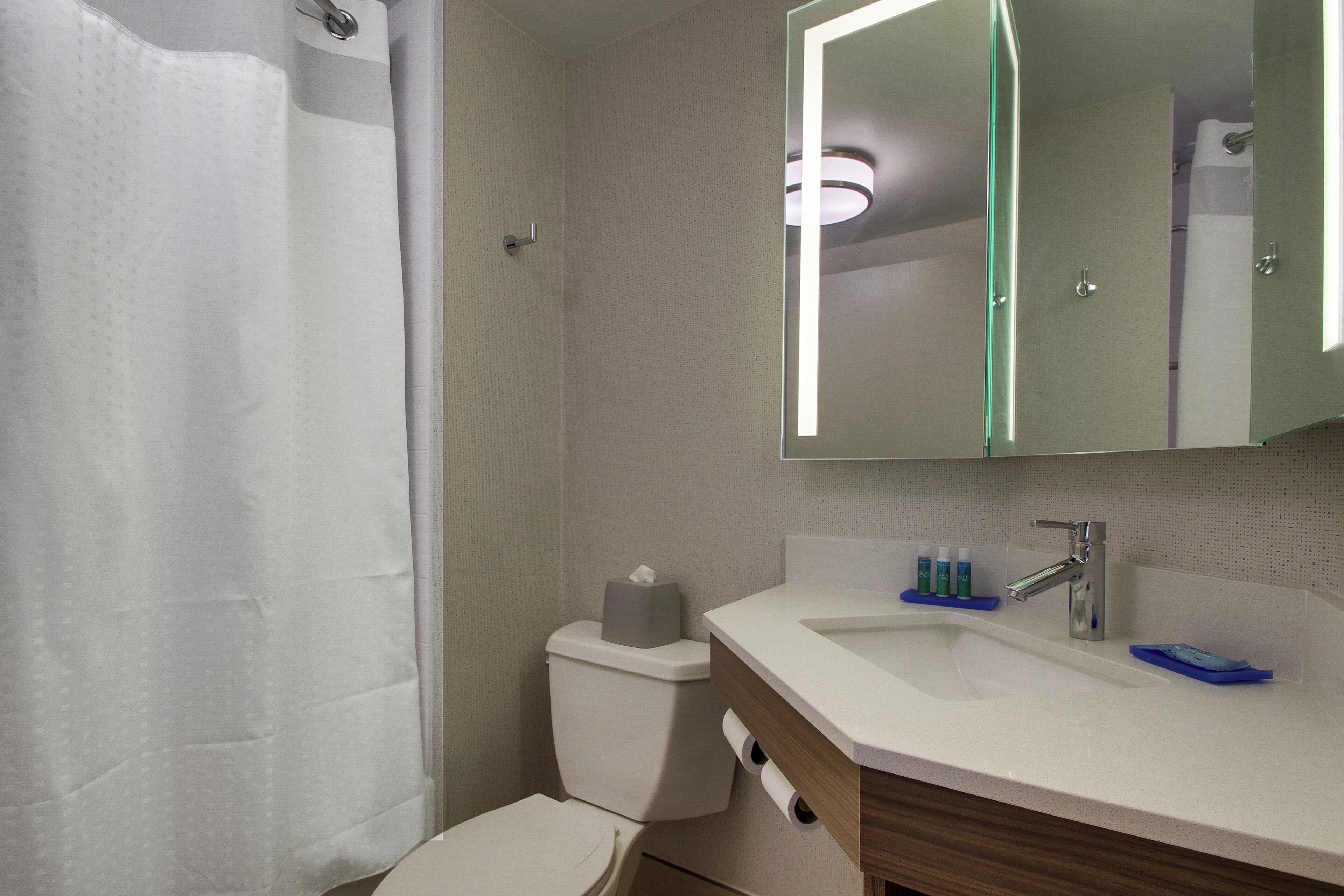 A bathroom with a shower, toilet, sink, and mirror.