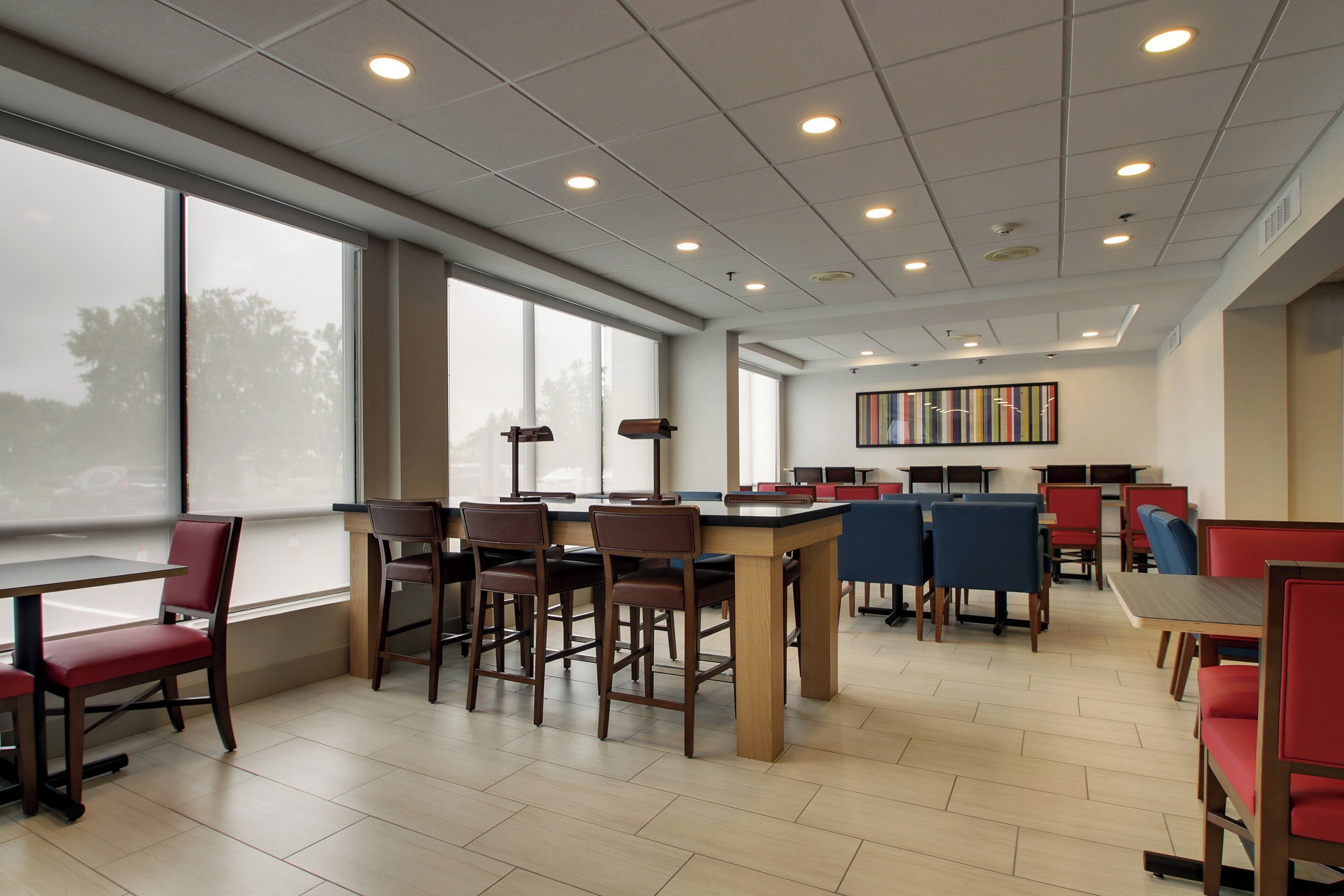 A modern library with multiple tables and chairs, large windows, and a ceiling with recessed lighting.