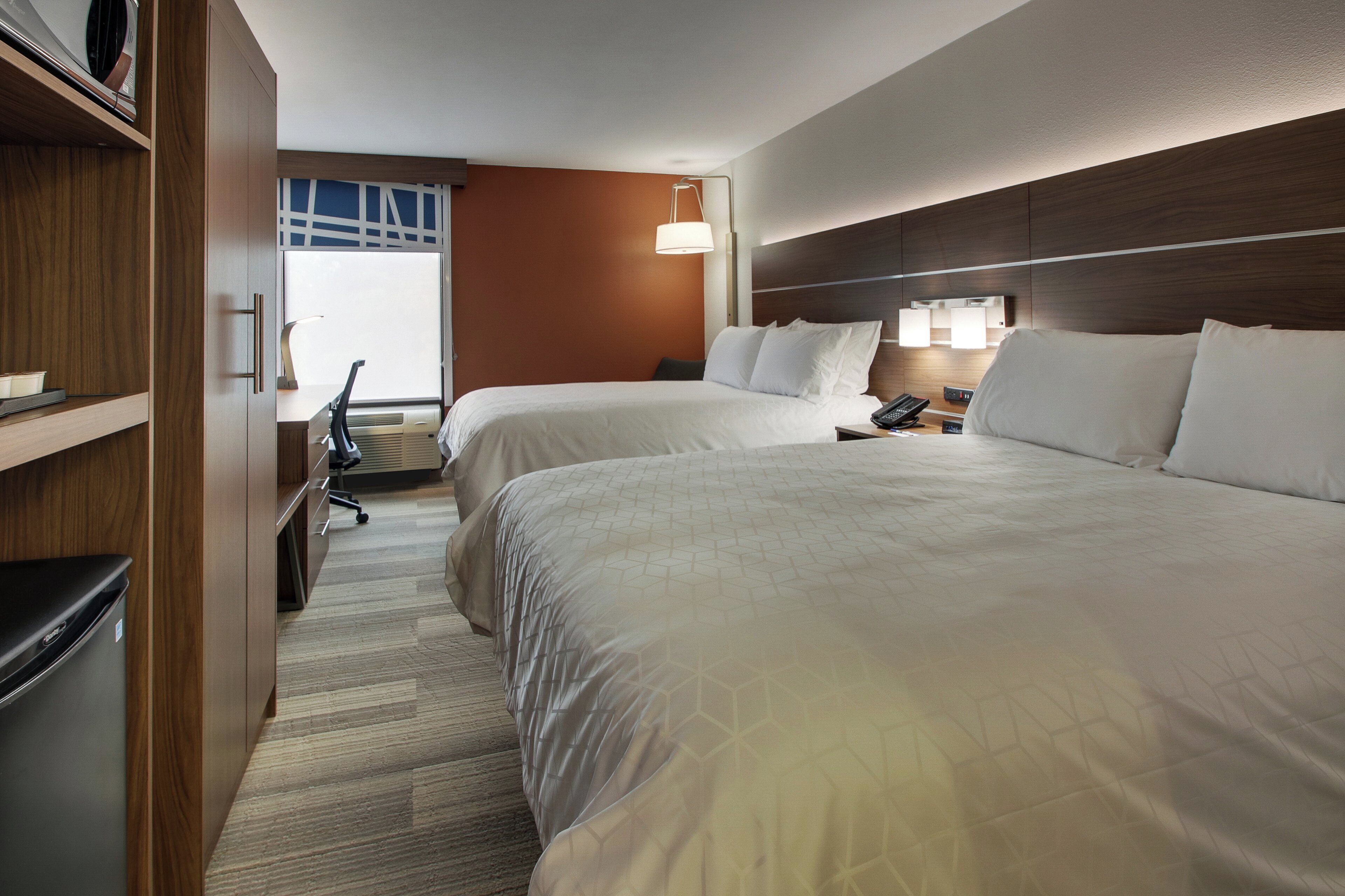 A hotel room with two beds, a desk, a chair, and a window.