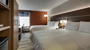 A hotel room with two beds, a desk with a chair, a lamp, and a view of the outdoors.