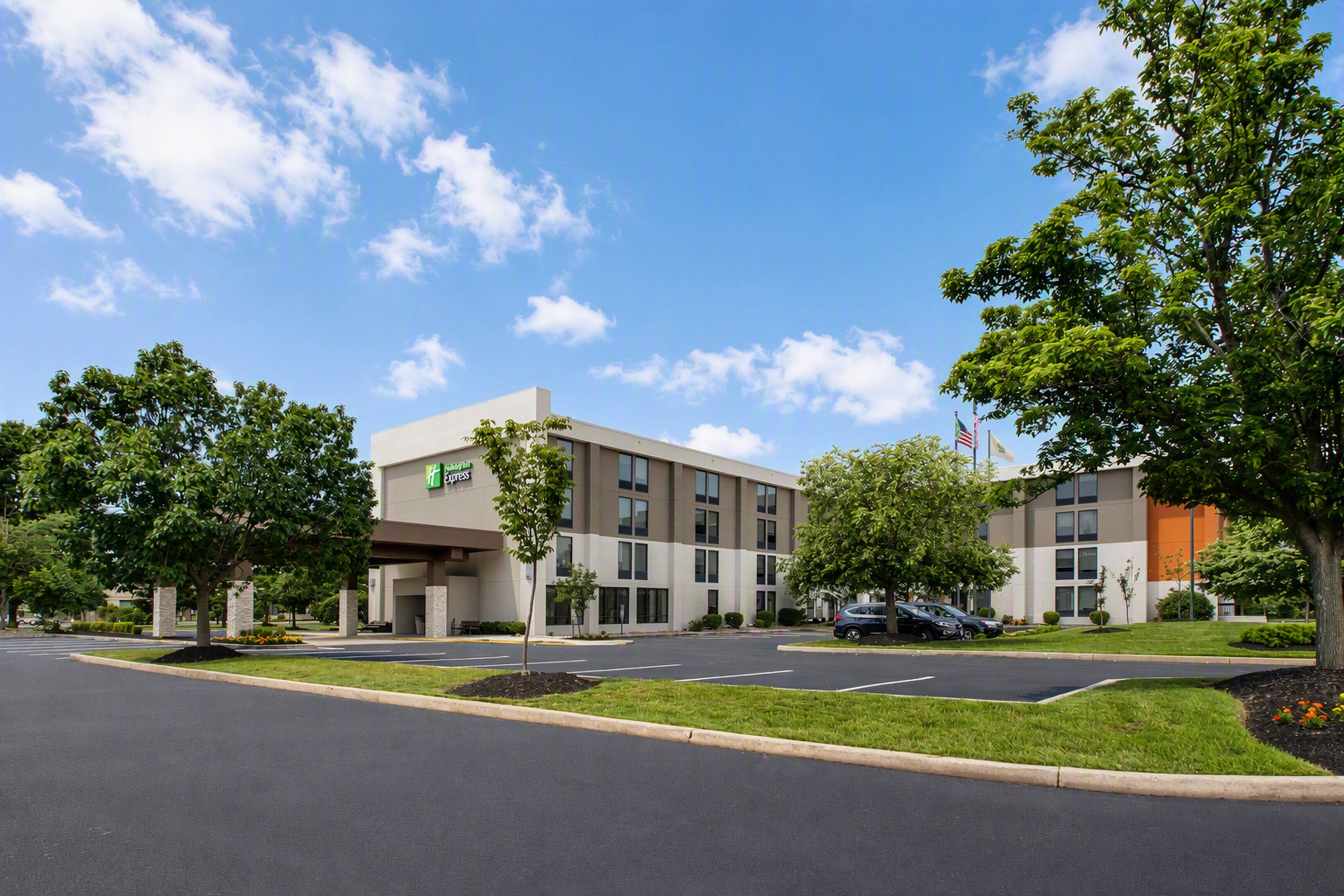 A modern hotel building with a flat roof, multiple windows, and a parking lot with cars.
