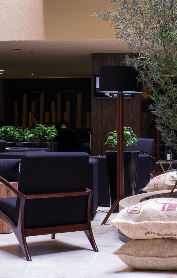 Un lobby moderno con muebles en tonos oscuros, una lámpara de pie grande y plantas en macetas.
