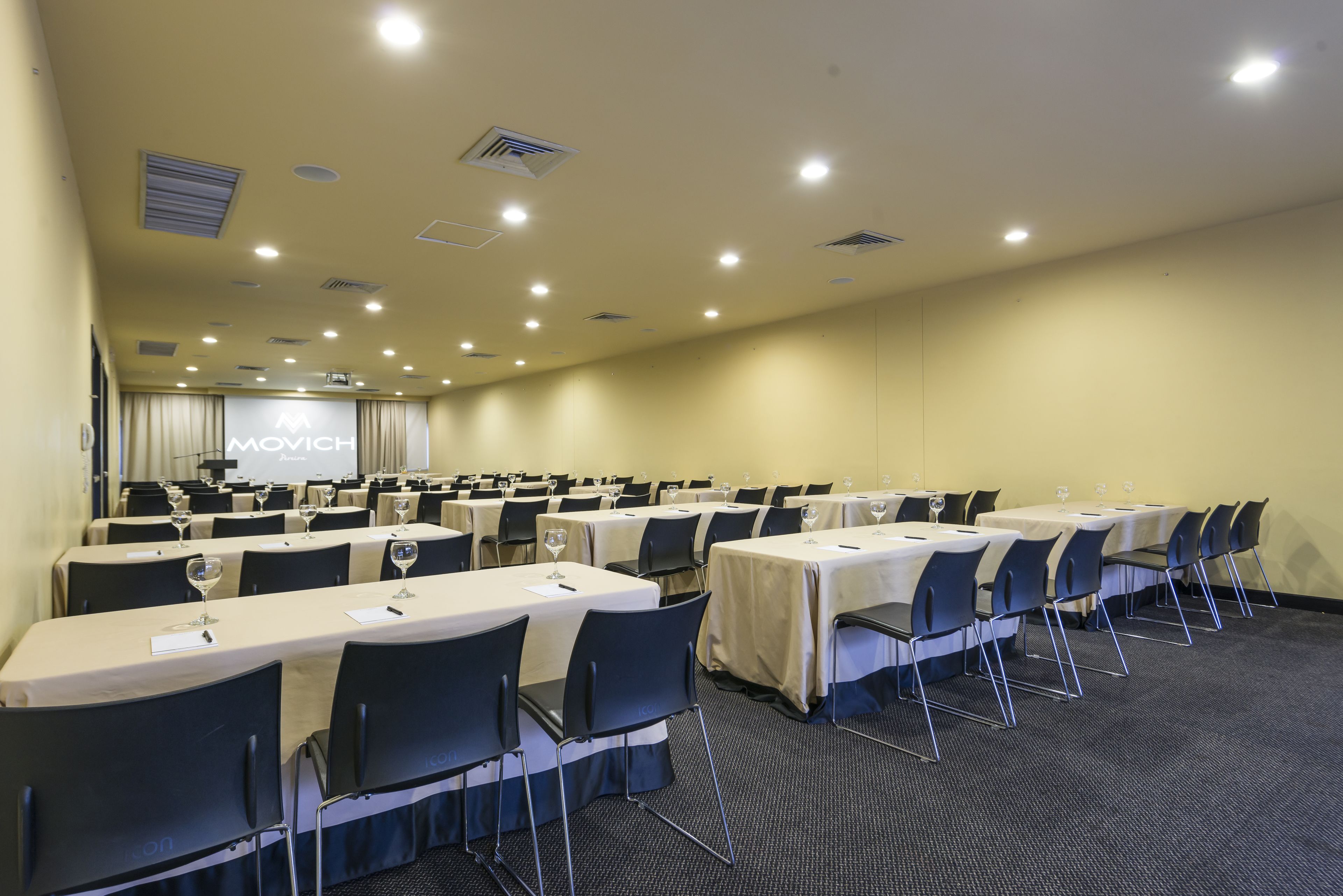 Un salón de conferencias con varias mesas, sillas y una pantalla de proyección.
