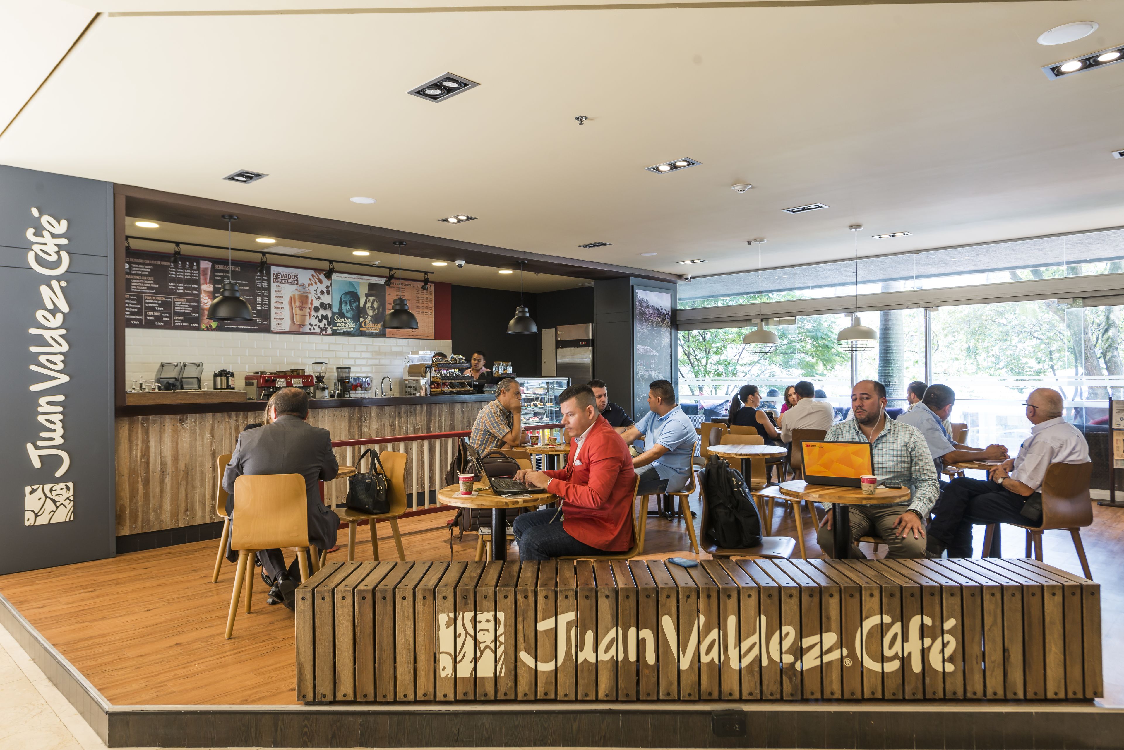 A modern cafe interior with wooden seating, a counter with a menu, and large windows allowing natural light.