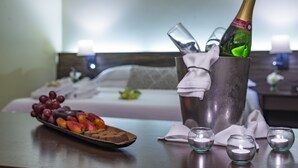 Une chambre d’hôtel avec un lit, une table de chevet sur laquelle se trouve une bouteille de champagne, une assiette de fruits et des bougies.