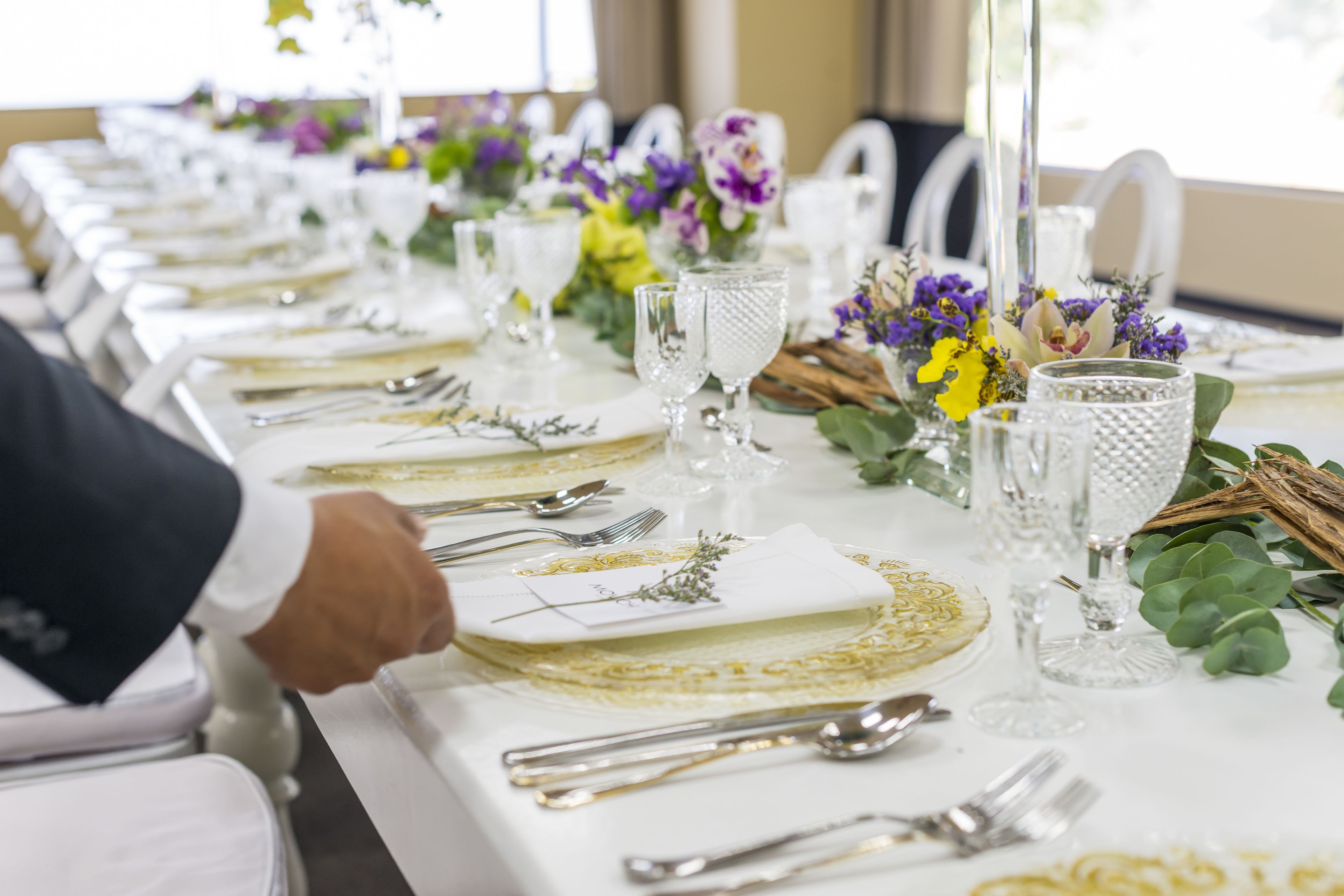 Una larga mesa de comedor vestida con manteles blancos, detalles dorados y centros de mesa florales.