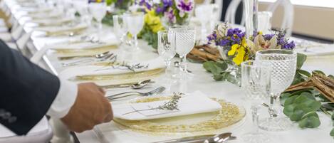 Una larga mesa de comedor vestida con manteles blancos, detalles dorados y centros de mesa florales.