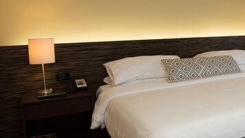 A neatly made bed with a patterned pillow, a bedside lamp, and a small bedside table with a phone and a magazine.