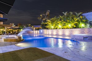 A nighttime pool area with a water feature, palm trees, and outdoor seating.