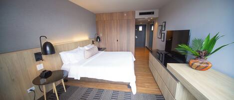 A hotel room with a bed, bedside tables, a desk, a TV, and a potted plant.