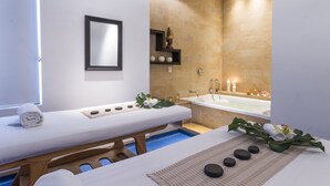 Une salle de spa moderne équipée d’une table de massage, d’une baignoire et d’une petite étagère où sont disposés des objets décoratifs.